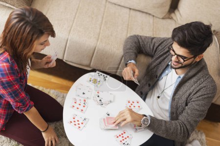 Téléchargez les photos : Couple assis sur le sol du salon à côté d'une table basse et s'amuser à jouer aux cartes - en image libre de droit