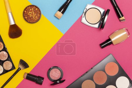 Foto de Disposición plana de varios productos de maquillaje sobre un fondo colorido con espacio de copia. Maquillaje de pinceles, coloretes, polvos faciales, corrector y iluminadores - Imagen libre de derechos
