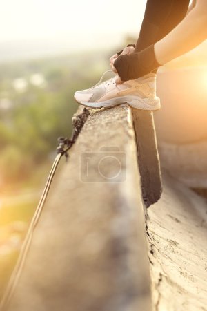 Foto de Mujer usando ropa deportiva de pie en una terraza de la azotea del edificio, atando cordones de zapatos antes del entrenamiento - Imagen libre de derechos