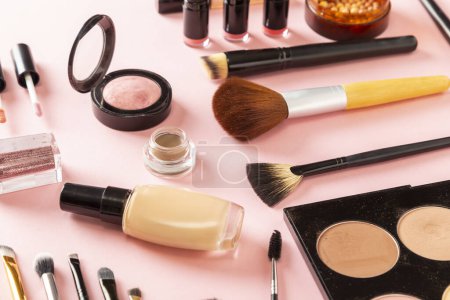 Foto de Vista de ángulo alto de varios productos de maquillaje sobre fondo rosa. Maquillaje de pinceles, coloretes, polvos faciales, iluminadores, brillo de labios, lápiz labial y purpurina - Imagen libre de derechos