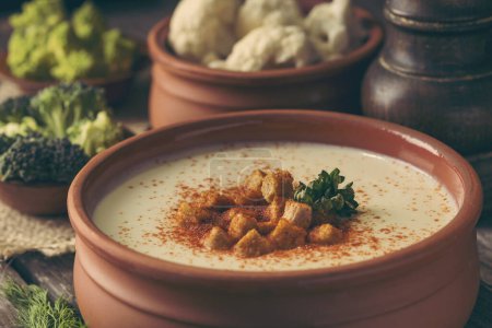 Photo for Bowl of cauliflower cream soup decorated with grounded red pepper and some croutons on a rustic wooden table. Selective focus on the croutons - Royalty Free Image