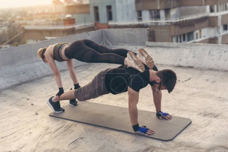 Téléchargez les photos : Couple travaillant sur un toit-terrasse du bâtiment, faisant un exercice de planche à bras droit. Concentrez-vous sur le gars - en image libre de droit