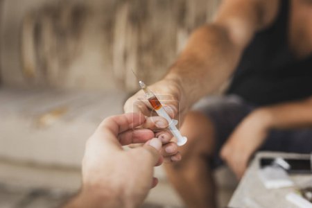 Téléchargez les photos : Détail des mains de deux utilisateurs de drogues intraveineuses partageant une seringue d'héroïne ; junkies tirant avec de l'héroïne - en image libre de droit