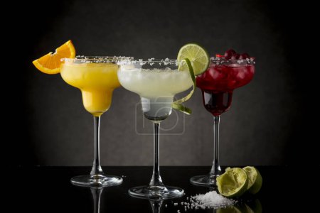 Photo for Classic lime margarita, orange margarita and cherry margarita cocktail mix in salt rimmed glasses garnished with slices of lime, orange and cherries - Royalty Free Image