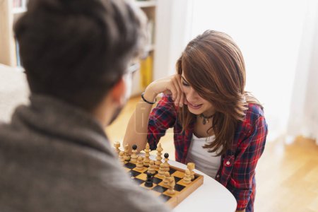 Téléchargez les photos : Couple amoureux assis sur le sol d'un salon, jouant aux échecs et s'amusant - en image libre de droit