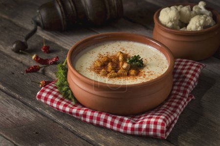 Photo for Bowl of cauliflower cream soup decorated with grounded red pepper and some croutons on a rustic wooden table. Selective focus - Royalty Free Image