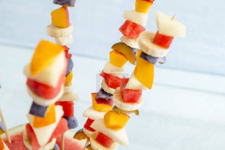 Foto de Detalle de una colorida ensalada mixta de frutas de temporada servida en palitos de barbacoa, pegada en una mitad de sandía como postre de fiesta de verano - Imagen libre de derechos
