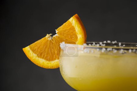 Photo for Detail of an orange margarita cocktail with tequila, triple sec, orange juice, crushed ice and some salt on the rim of a glass, decorated with a slice of orange - Royalty Free Image