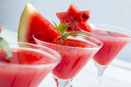 Photo for Detail of cold watermelon cocktails in martini glasses decorated with slices of watermelon and mint leaves. Selective focus on the mint leaves - Royalty Free Image