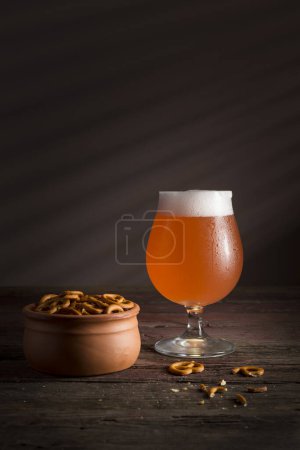 Foto de Vaso de cerveza de pomelo fría con un tazón de pretzels en una mesa de madera rústica - Imagen libre de derechos