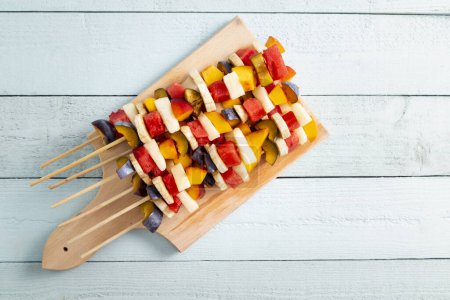 Foto de Mesa de plano de una colorida ensalada de frutas mixtas frías servida en palitos de barbacoa como postre de verano - Imagen libre de derechos