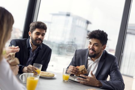 Téléchargez les photos : Groupe de gens d'affaires prenant le petit déjeuner dans le restaurant de l'entreprise. Concentrez-vous sur l'homme à droite - en image libre de droit