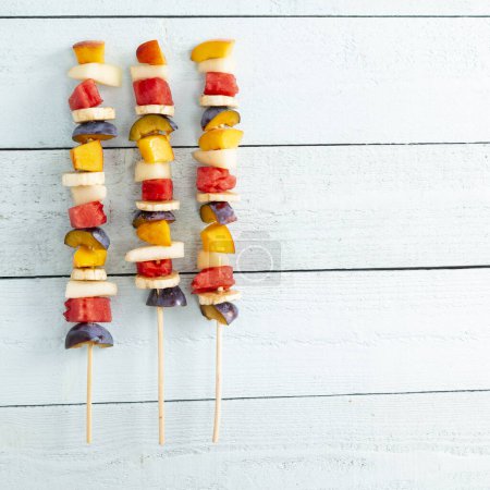 Téléchargez les photos : Plan de table de salade de fruits mélangés colorés froids servis sur des bâtonnets de barbecue comme dessert estival - en image libre de droit