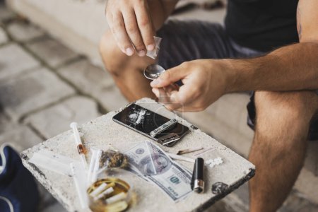 Foto de Detalle de manos masculinas añadiendo heroína a una cuchara, preparándola para uso intravenoso - Imagen libre de derechos