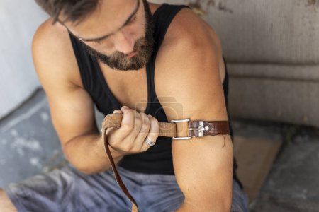Foto de Junco intravenoso aplicando un cinturón como torniquete antes de inyectarse heroína. Concéntrate en el cinturón - Imagen libre de derechos