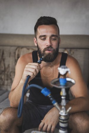 Téléchargez les photos : Homme inhalant du tabac aromatisé fruité à base de mélasse à l'aide d'une pipe à eau, d'un narguilé ou d'un narghile - en image libre de droit