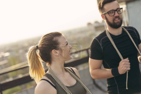 Téléchargez les photos : Couple debout sur un toit-terrasse du bâtiment, se préparer pour l'exercice avec des cordes. Concentre-toi sur la fille - en image libre de droit