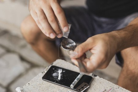 Téléchargez les photos : Détail des mains masculines ajoutant de l'héroïne à une cuillère, le préparant pour une utilisation intraveineuse - en image libre de droit