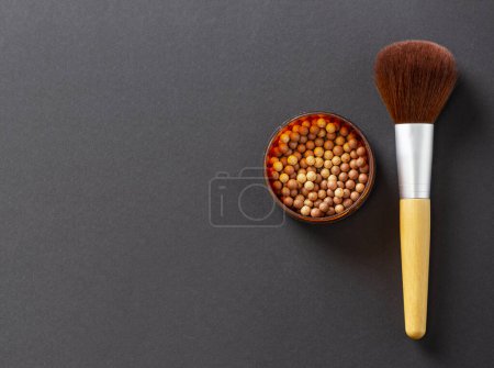 Photo for Flat lay of face powder pearls in an open powder box and a make up brush isolated on black background with copy space. Selective focus on the pearls - Royalty Free Image