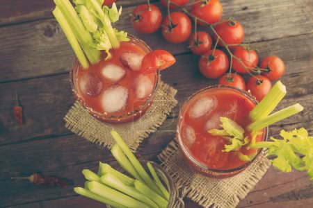 Foto de Mesa de copa de cóctel Bloody Mary con vodka, zumo de limón y tomate, salsa de tabasco y cubitos de hielo decorados con hojas de apio. Concéntrate en la parte superior de las gafas - Imagen libre de derechos