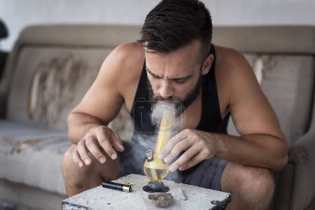 Foto de Hombre joven fumando marihuana usando pipa; hombre inhalando vapor de marihuana de una pipa - Imagen libre de derechos