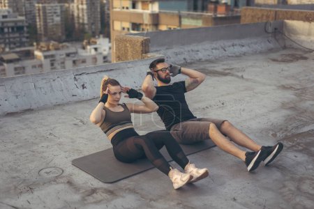 Photo for Couple wearing sportswear doing sit ups on a building rooftop terrace - Royalty Free Image