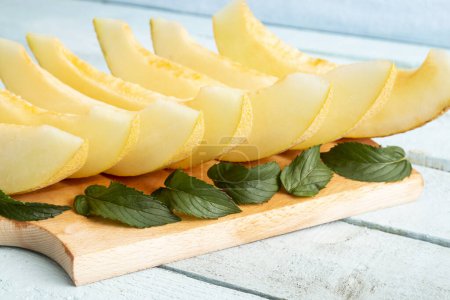 Foto de Rebanadas frías de melón servidas en una tabla de cortar, decoradas con hojas de menta, servidas como postre de verano. Enfoque selectivo - Imagen libre de derechos