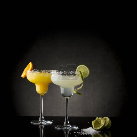 Téléchargez les photos : Mélange classique de margarita au citron vert et de margarita à l'orange dans des verres à bordure de sel garnis de tranches de citron vert et d'orange - en image libre de droit