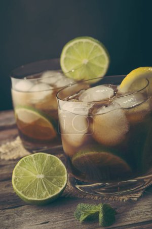 Téléchargez les photos : Deux verres de Cuba Libre Cocktail avec rhum, coke, jus de citron et glaçons sur une table en bois rustique. Focus sélectif sur le verre au premier plan - en image libre de droit