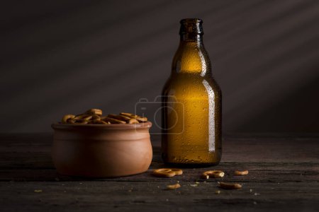 Foto de Botella de cerveza húmeda bien refrigerada y un tazón de pretzels colocado en una mesa de madera rústica en un bar - Imagen libre de derechos