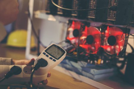 Photo for Detail of male hand holding a wattmeter measuring cryptocurrency mining rig electrical energy consumption. Selective focus on the wattmeter - Royalty Free Image