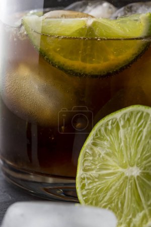 Foto de Primer plano de un cóctel Cuba Libre con ron integral, zumo de limón, coque y cubitos de hielo, decorado con rodajas de lima fresca. Enfoque selectivo - Imagen libre de derechos