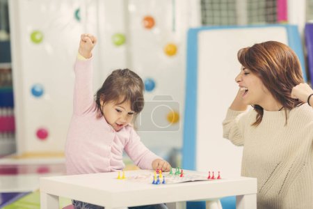 Téléchargez les photos : Mère et fille assises dans une salle de jeux, jouant à un jeu de ludo ; fille heureuse parce qu'elle a gagné le jeu. Focus sur la fille - en image libre de droit