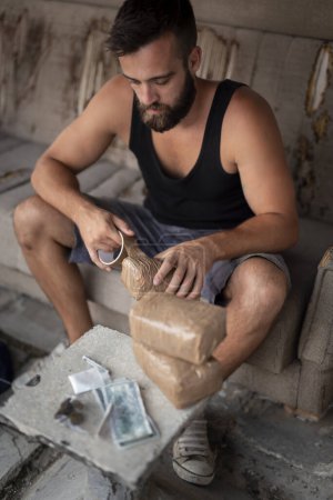 Photo for Drug trafficker taping heroin bricks and packing goods for transportation and sale. Focus on the heroin brick being taped - Royalty Free Image