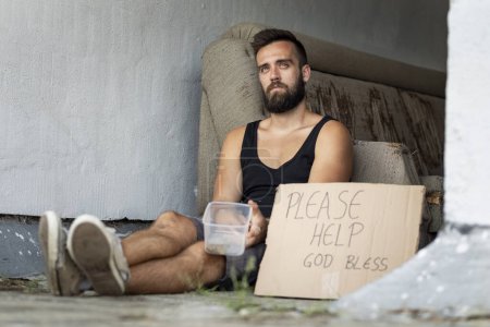 Foto de Un vagabundo sentado en la calle, pidiendo dinero - Imagen libre de derechos