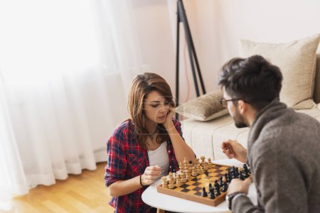 Téléchargez les photos : Couple amoureux assis sur le sol d'un salon, jouant aux échecs et s'amusant - en image libre de droit
