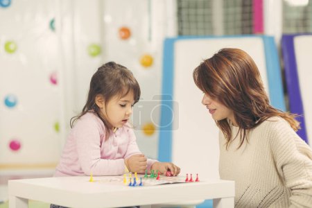 Téléchargez les photos : Mère et fille assises dans une salle de jeux, jouant à un jeu de ludo et profitant de leur temps ensemble - en image libre de droit