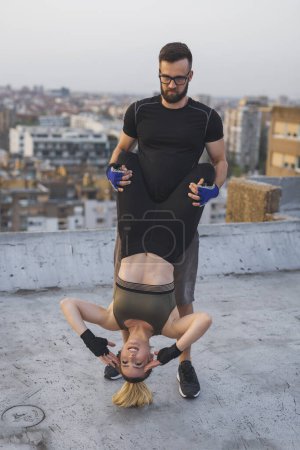 Téléchargez les photos : Couple portant des vêtements de sport faisant de l'exercice de craquements suspendus sur un toit-terrasse du bâtiment - en image libre de droit