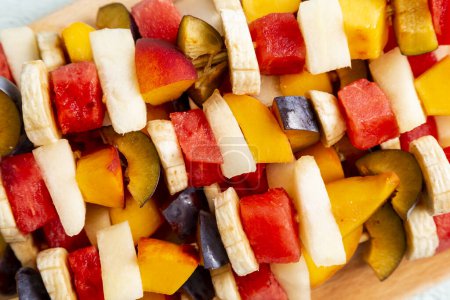 Téléchargez les photos : Salade de fruits mélangés colorés servis sur bâtonnets de barbecue. Concentration sélective - en image libre de droit