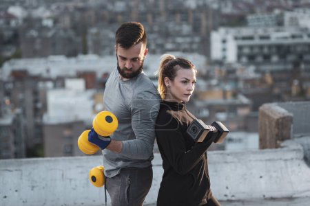 Photo for Young couple working out on a building rooftop terrace, lifting weights, doing arms exercises - Royalty Free Image