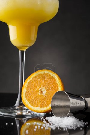Photo for Orange margarita cocktail with tequila, triple sec, orange juice, crushed ice and some salt on the rim of a glass, decorated with a slice of orange. Selective focus on the jigger numbers scale - Royalty Free Image