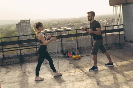 Foto de Pareja de pie en una terraza de la azotea del edificio, haciendo ejercicio con cuerdas. Concéntrate en el tipo - Imagen libre de derechos