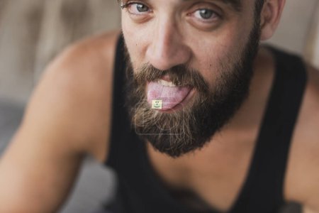 Téléchargez les photos : Jeune homme prenant du LSD ; timbre LSD sur la langue de l'homme - en image libre de droit