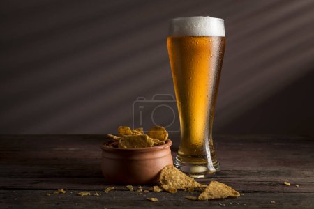Téléchargez les photos : Verre de bière froide pâle avec un bol de copeaux de tortilla sur une table en bois rustique - en image libre de droit