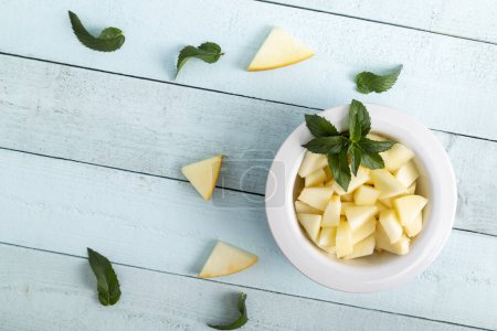 Photo for Table top shot of a bowl of cold melon slices decorated with mint leaves. Focus on the mint leaves and melon slices in the bowl - Royalty Free Image