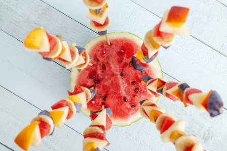 Photo for Table top shot of a colorful mixed seasonal fruit salad served on barbecue sticks, stuck in a watermelon half as a summer party dessert - Royalty Free Image