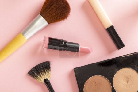 Téléchargez les photos : Plan de table des produits de maquillage, de beauté et de cosmétiques isolés sur fond rose. Brosses de maquillage, rouge à lèvres, rouge à lèvres et surligneur de visage palette - en image libre de droit