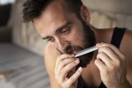 Young man rolling a joint, licking the rolling paper in order to seal it