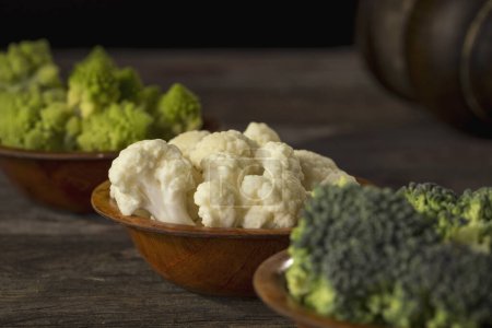 Photo for Fresh pieces of romanesco broccoli, broccoli and cauliflower in small rustic wooden bowls. Selective focus on the cauliflower - Royalty Free Image