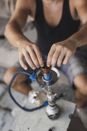 Photo for Man filling up the hookah with fruity flavored, molasses based eastern tobacco, getting it ready for use. - Royalty Free Image